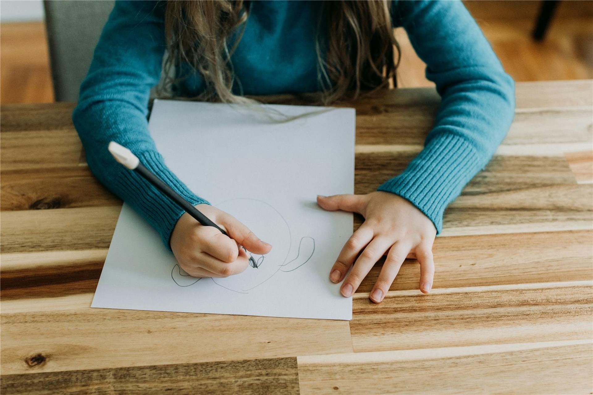 Ein braunhaariges Mädchen zeichnet mit Bleistift ein Gesicht auf Papier. 