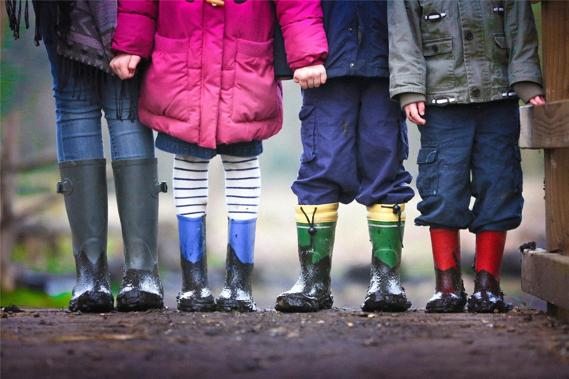 4 Kinder in Regensachen und Gummistiefeln halten sich an den Händen. Man sieht nur die Unterkörper und Beine der Kinder. 
