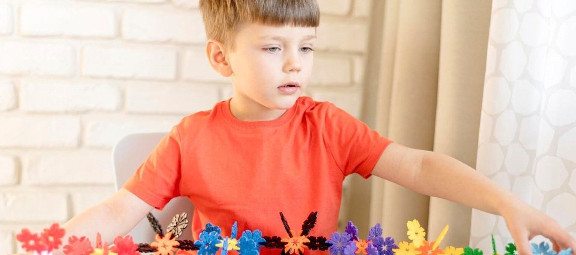 Ein etwa vierjähriger Junge mit braunen Haaren und in orangefarbenem T-Shirt spielt mit Plastiksteckspielzeug