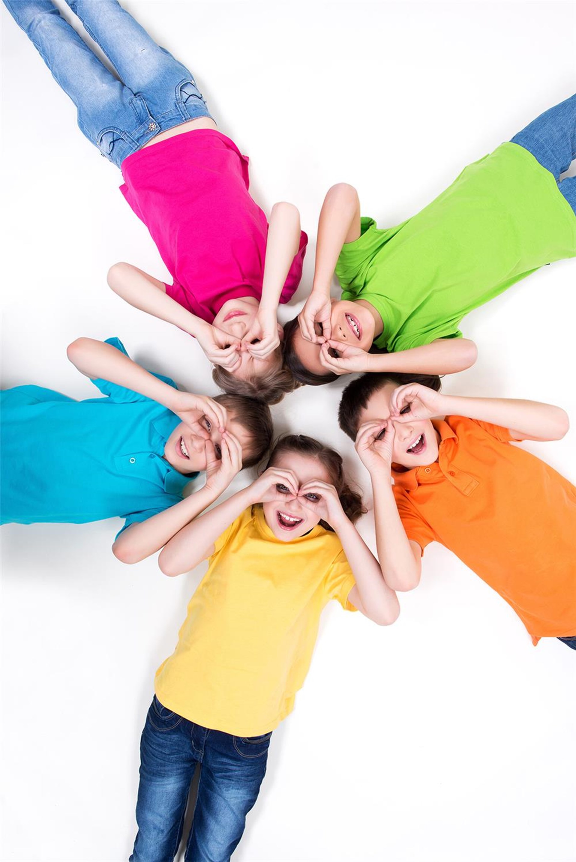 Fünf Kinder in bunten T-Shirts liegen auf dem Boden und formen mit den Händen eine Brille vor ihrem Gesicht. Das Foto zeigt sie von oben. 